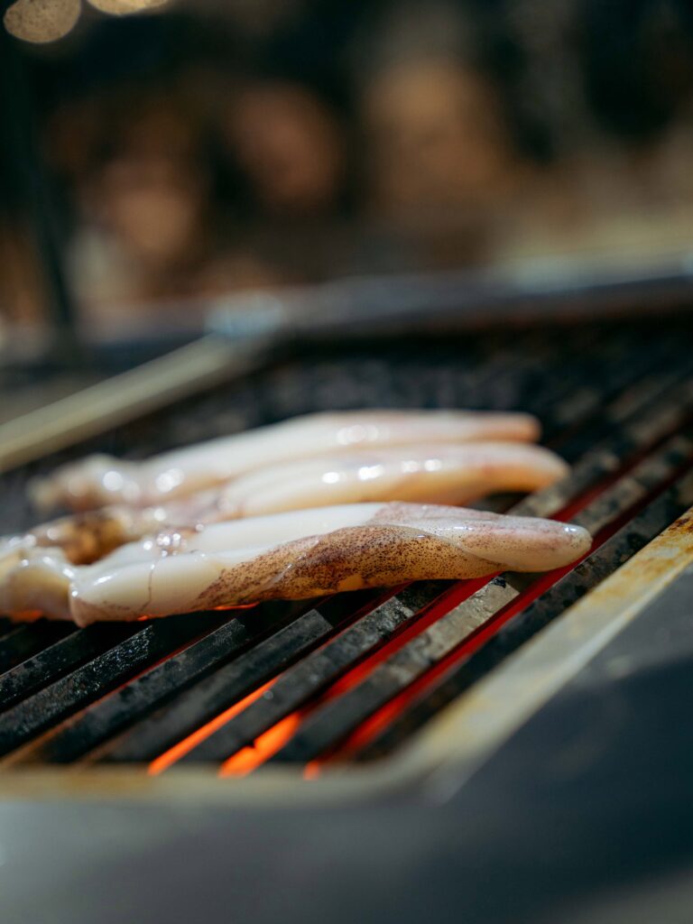 Shrimp skewers cooking on a barbecue grill with orange flames underneath.