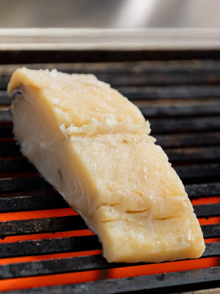 Piece of pale yellow cheese resting on a hot grill, with glowing orange grates beneath.