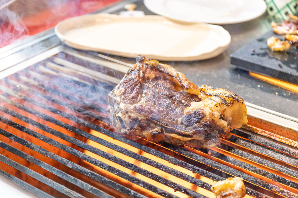 Beef steak grilling on a barbecue grill with orange flames and wisps of smoke.